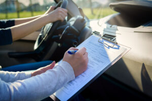 person writing notes while driver is taking driving test with hands on the wheel